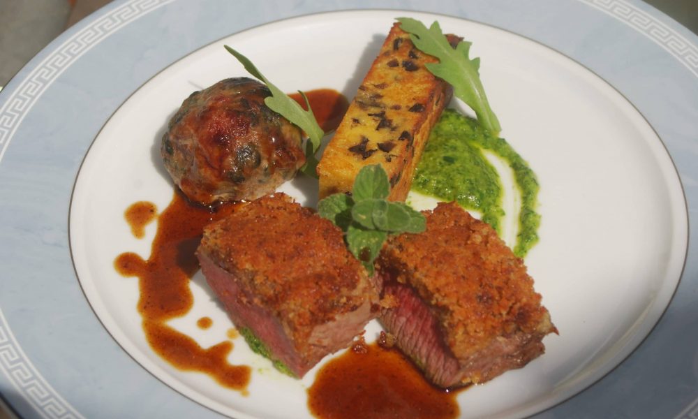 Selle d’agneau en croute de moutarde, caillette aux herbes, panisse aux olives, pesto de roquette, jus à la Nepita