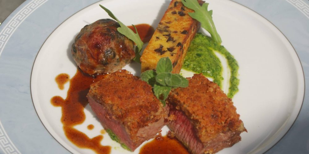 Selle d’agneau en croute de moutarde, caillette aux herbes, panisse aux olives, pesto de roquette, jus à la Nepita