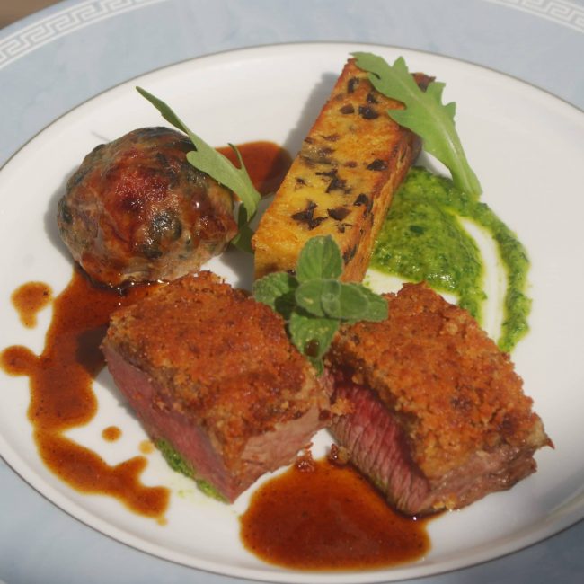 Selle d’agneau en croute de moutarde, caillette aux herbes, panisse aux olives, pesto de roquette, jus à la Nepita